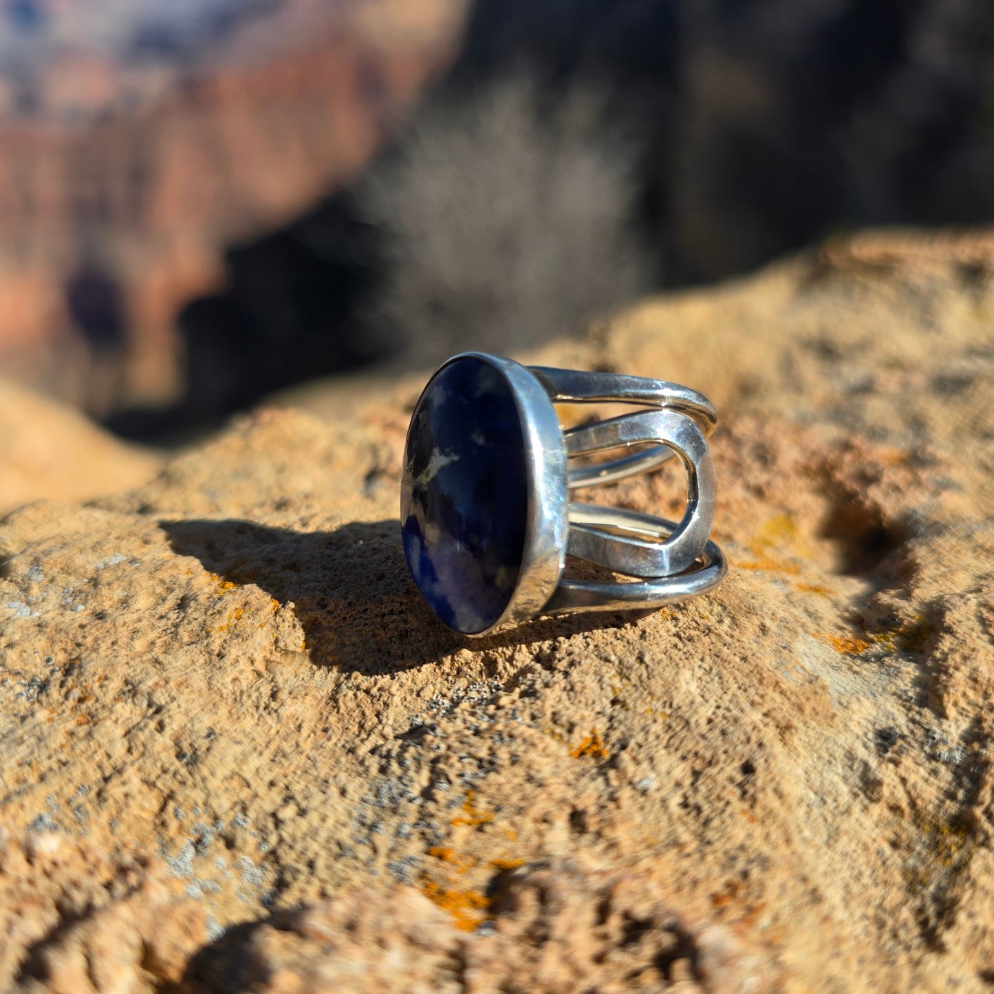 Adjustable blue sodalite ring featuring a smooth oval stone set in silver, shown against a natural surface angled view