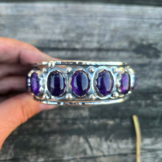 Large sterling silver cuff bracelet with multiple oval amethyst stones set across being held by hand top view.