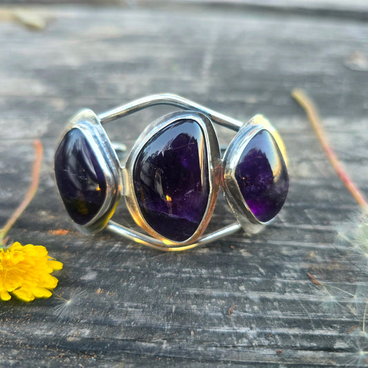 Wide sterling silver statement cuff bracelet with 3 large oval amethyst gemstones displayed on wood front view