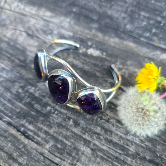 Wide sterling silver statement cuff bracelet with 3 large oval amethyst gemstones displayed on wood