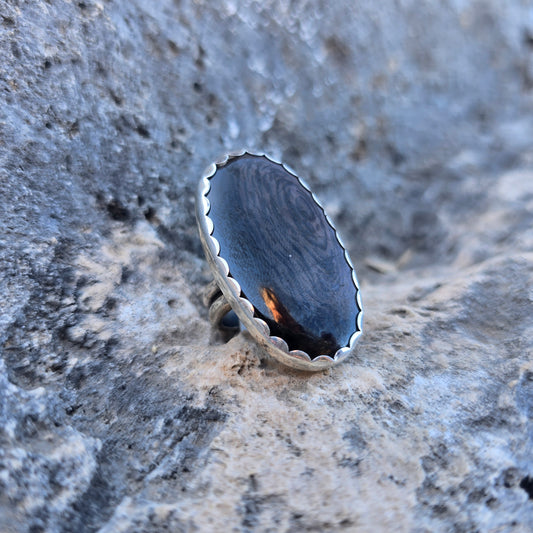 Oval psilomelane stone ring with a stone measuring just over 1.5 inches, set in a scalloped sterling silver bezel with an adjustable open band angled view.