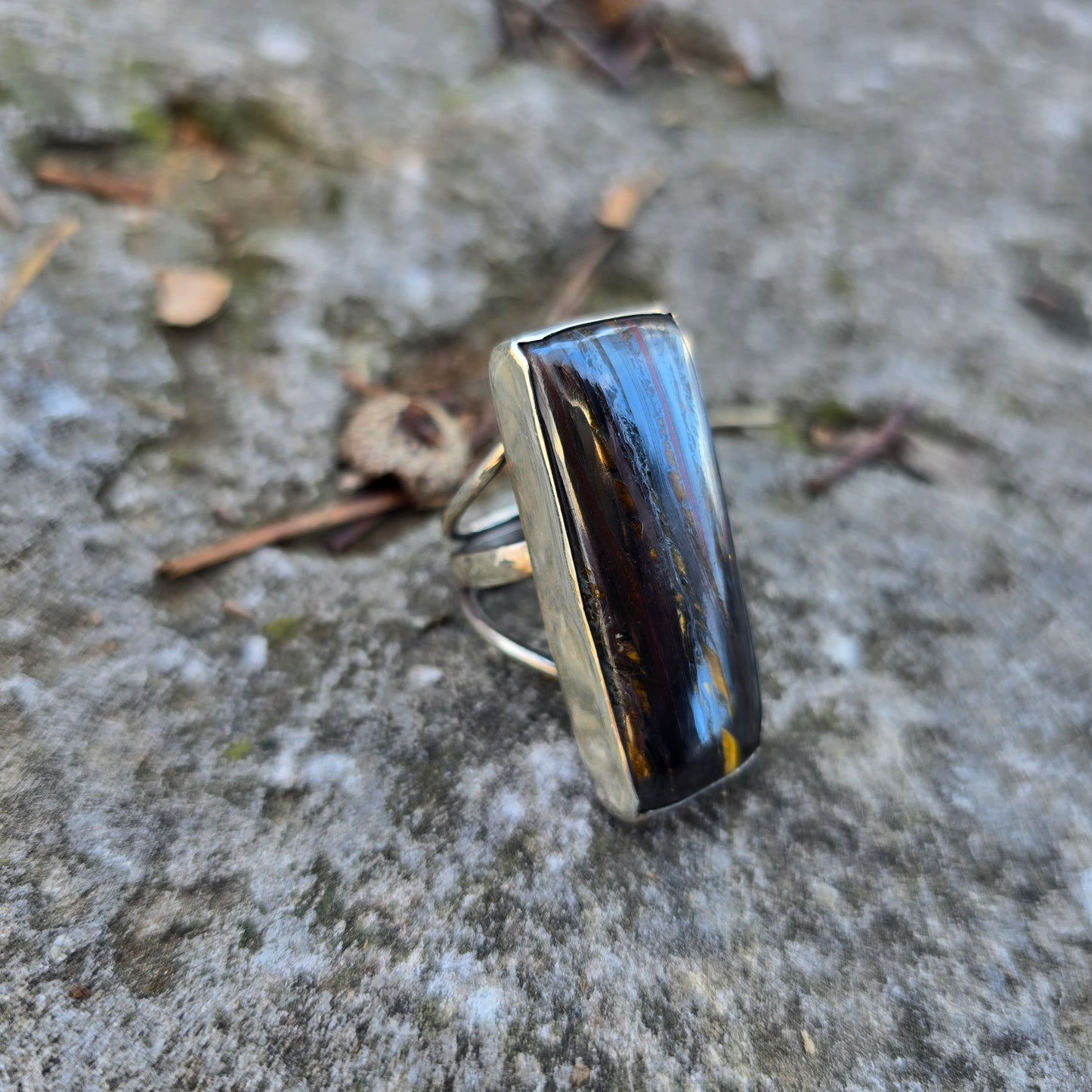 silver ring with tiger iron stone displayed on rock