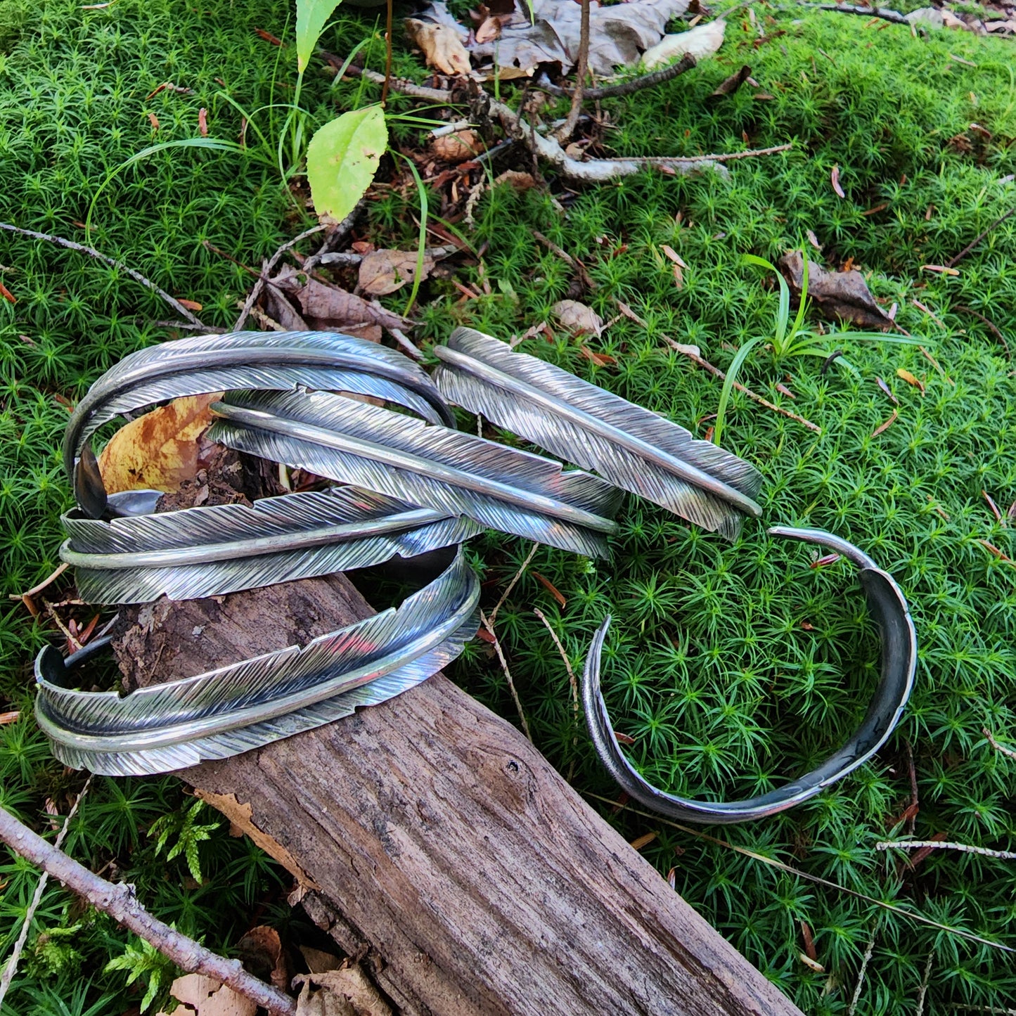 collection of feather cuff bracelets displayed on log on moss