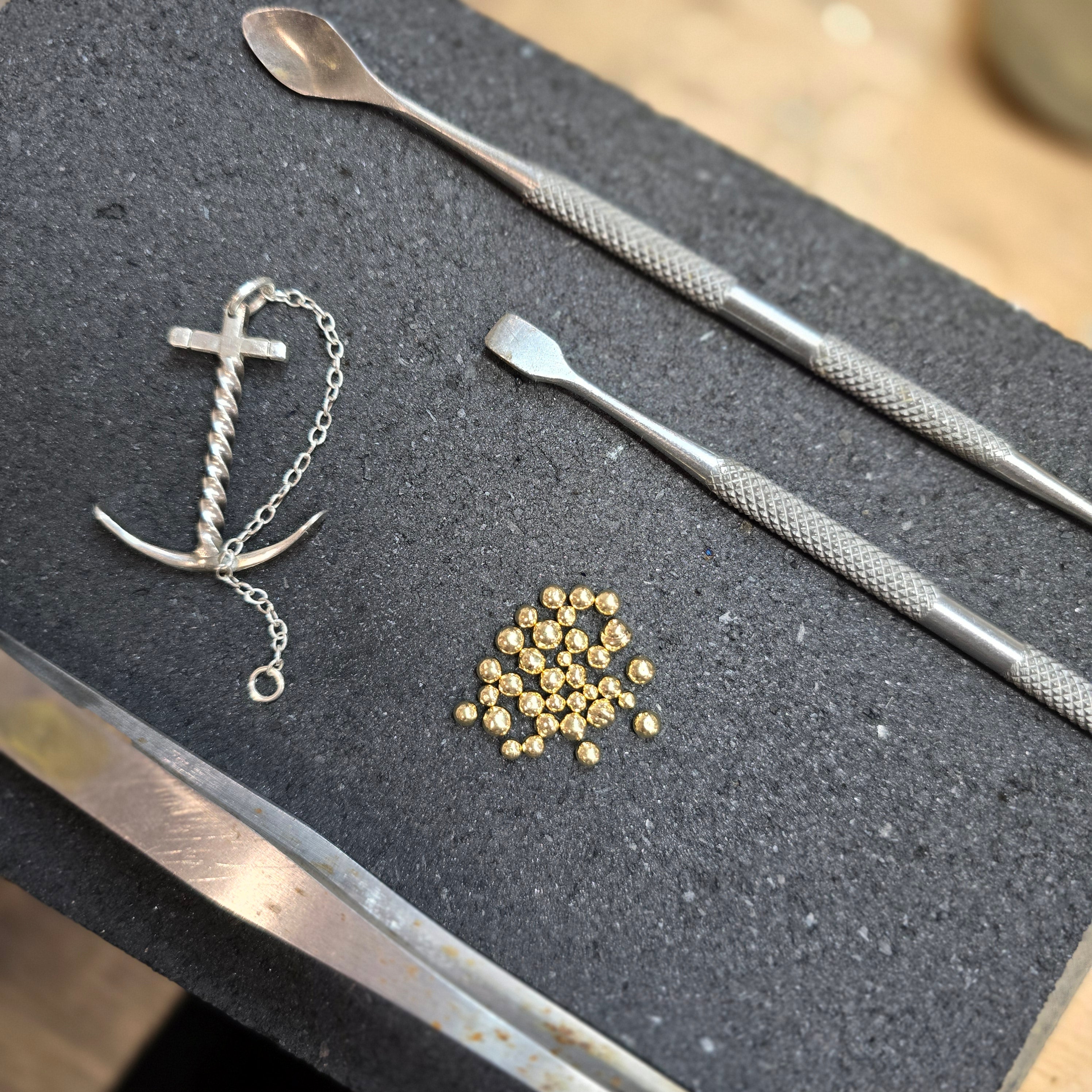 18k gold raw metal and sterling silver on bench of silversmiths soldering block.