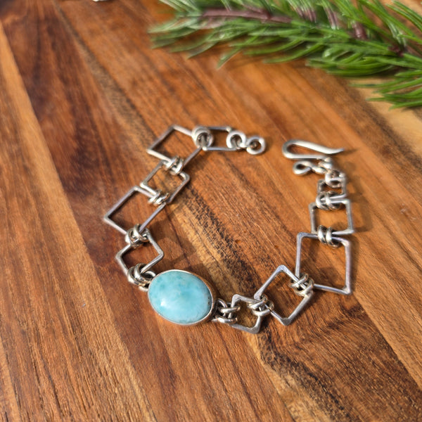 Larimar bracelet with square sterling silver components, displayed flat on a wooden surface in top view, showing rectangular larimar stones set within squared silver links