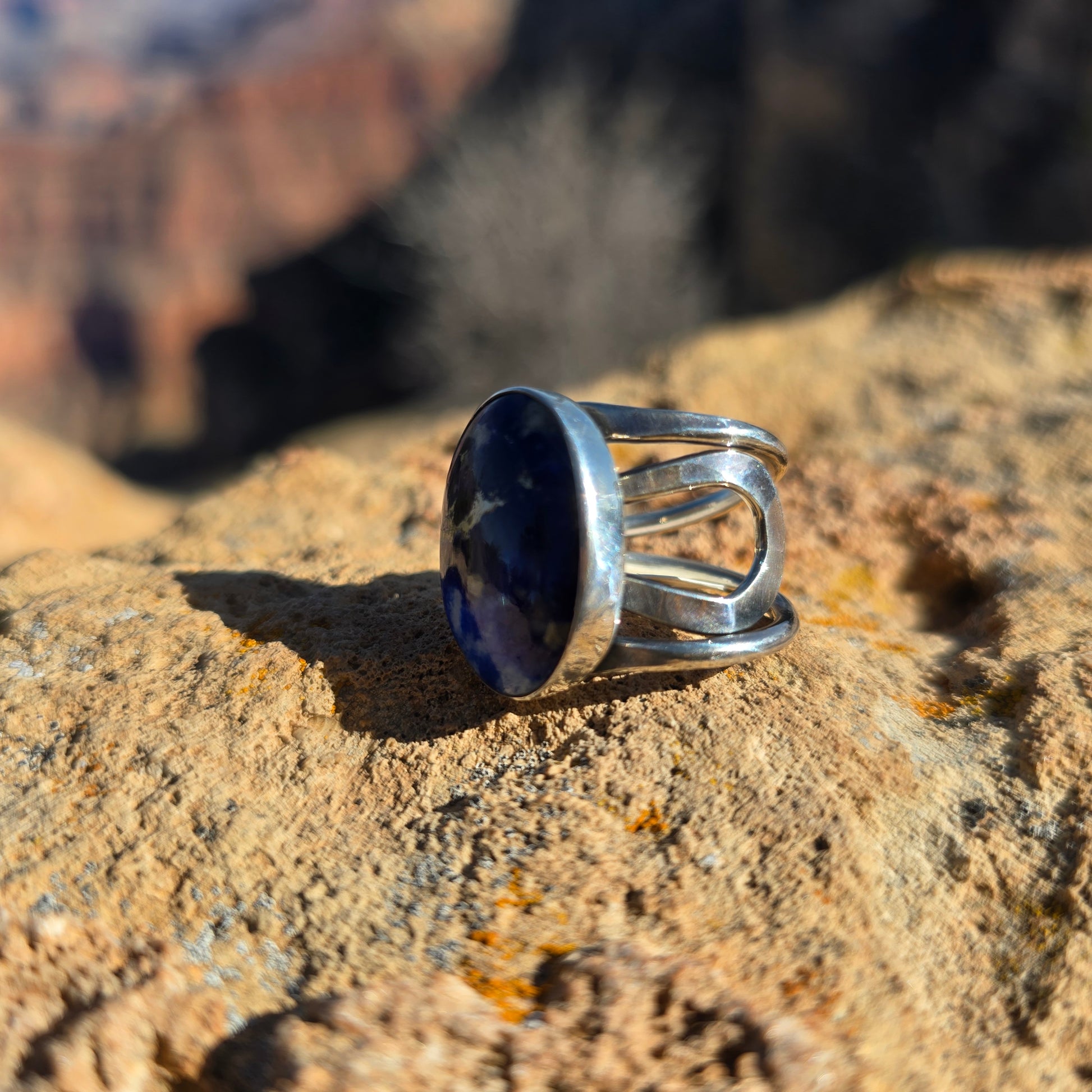 Adjustable blue sodalite ring featuring a smooth oval stone set in silver, shown against a natural surface angled view