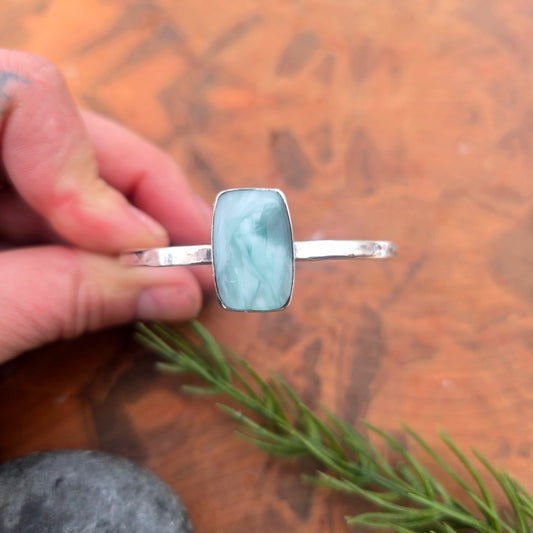 Aqua chalcedony cuff bracelet showing a rectangular chalcedony set in a smooth bezel on a single hammered silver cuff with hand holding for top view.