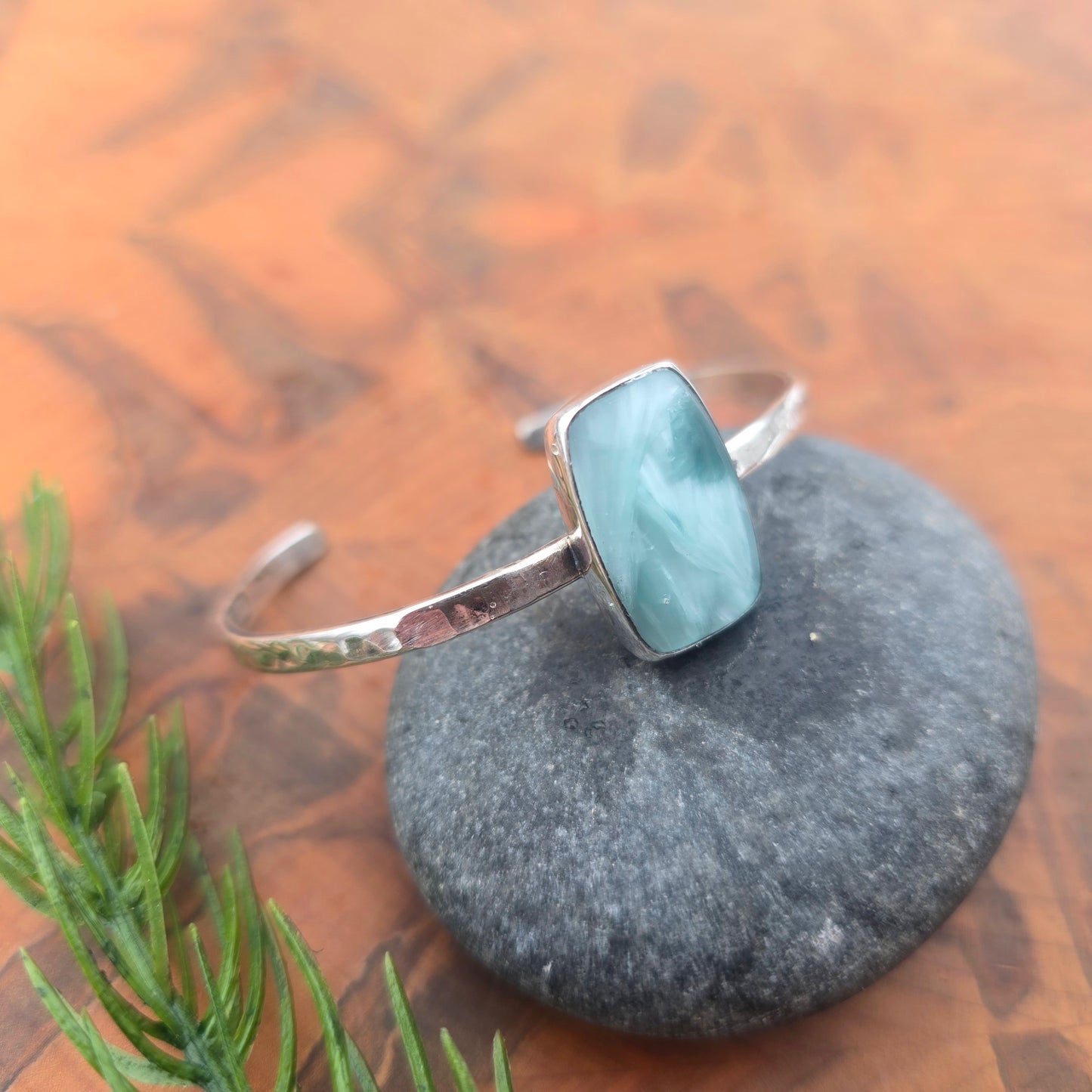 Sterling silver cuff featuring a rectangular aqua chalcedony stone, forged surface with hammer marks visible along the band displayed on rock angled top view.