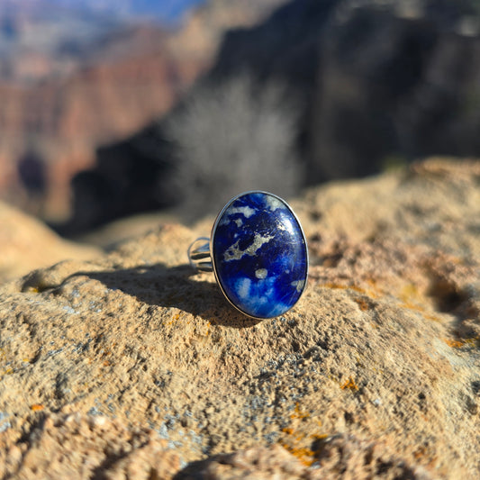 Blue sodalite ring with an oval stone set on a silver band, photographed on a natural background.