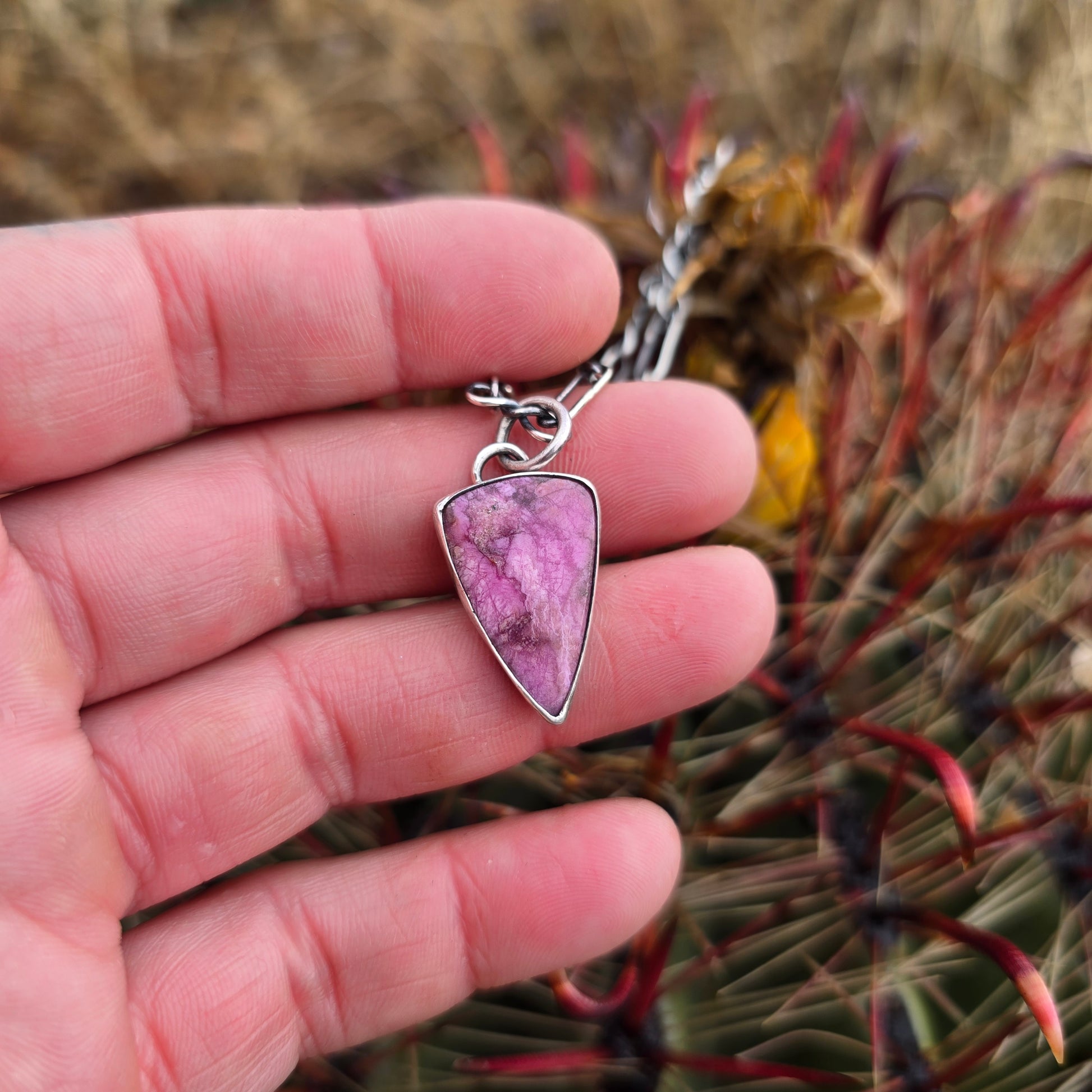 Shiny pink cobalto calcite pendant shaped into a clean triangle with crisp edges displayed on hand.
