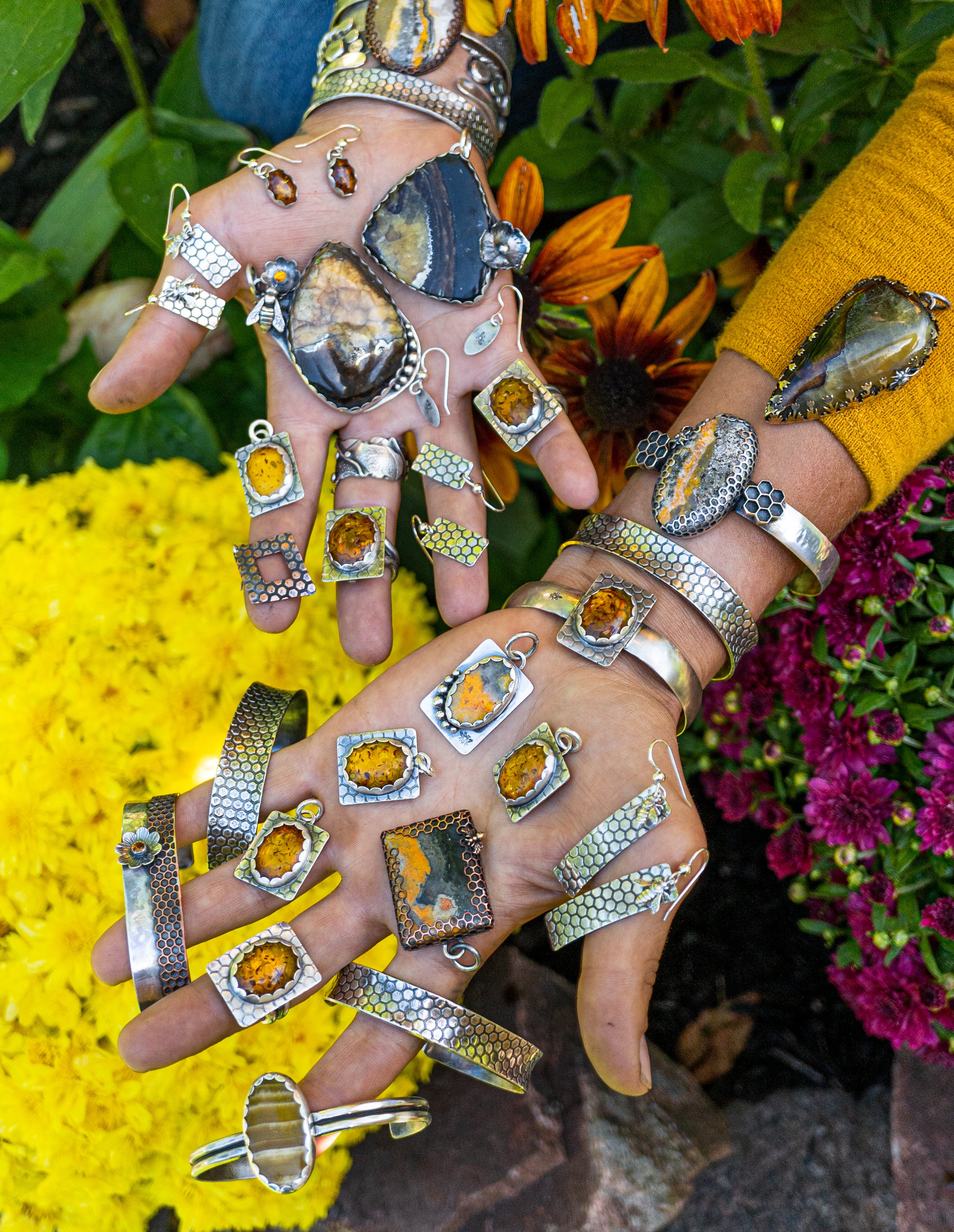 Collection of hand-forged sterling silver honey bee inspired jewelry displayed across silversmiths hands in natural setting.