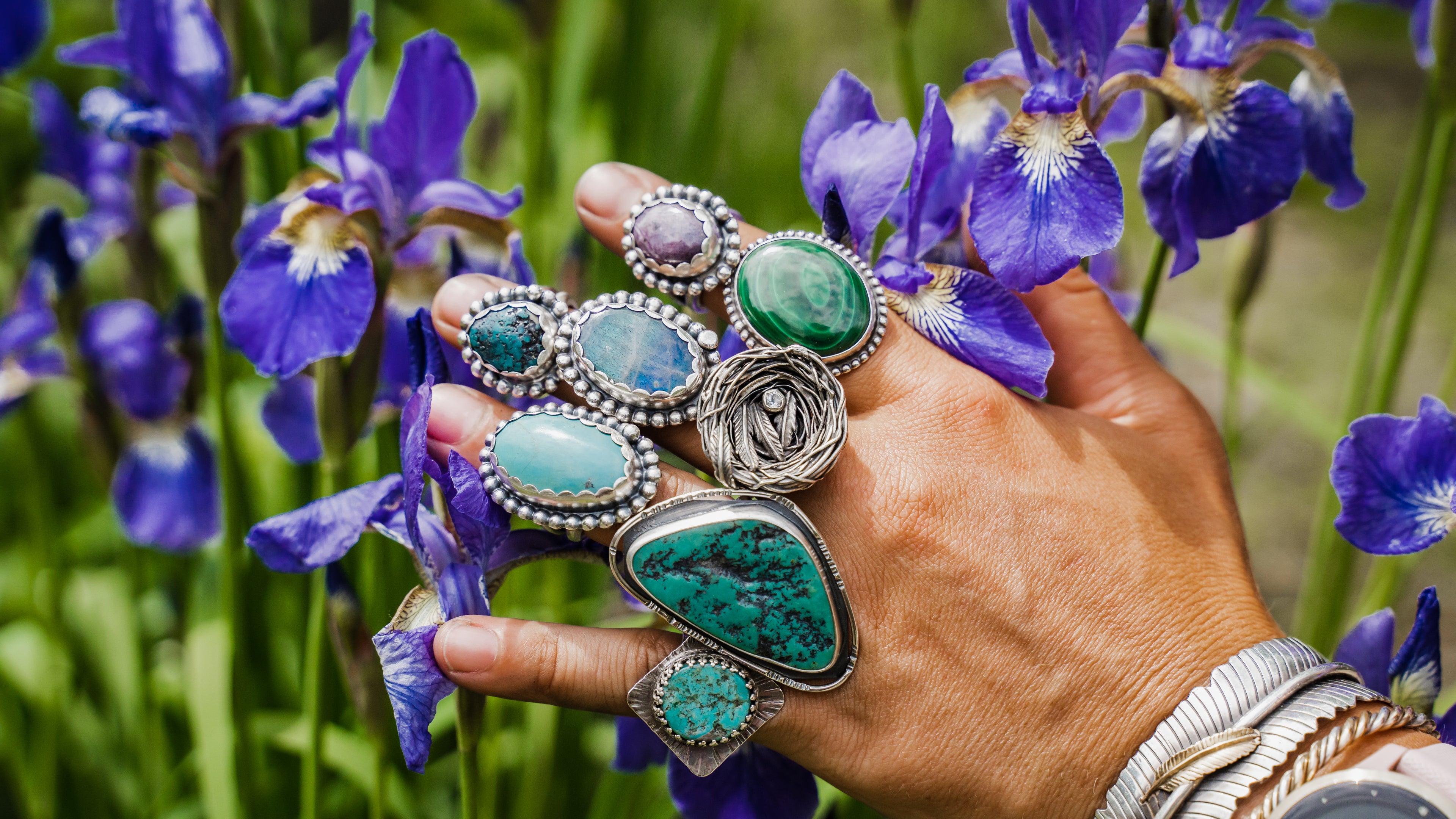 Collection of rings displayed on silversmiths Emily Dicobs hand with flowers in the background.