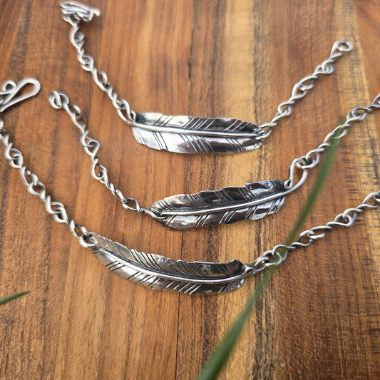 Collection of sterling silver feather bracelets on wooden surface top view