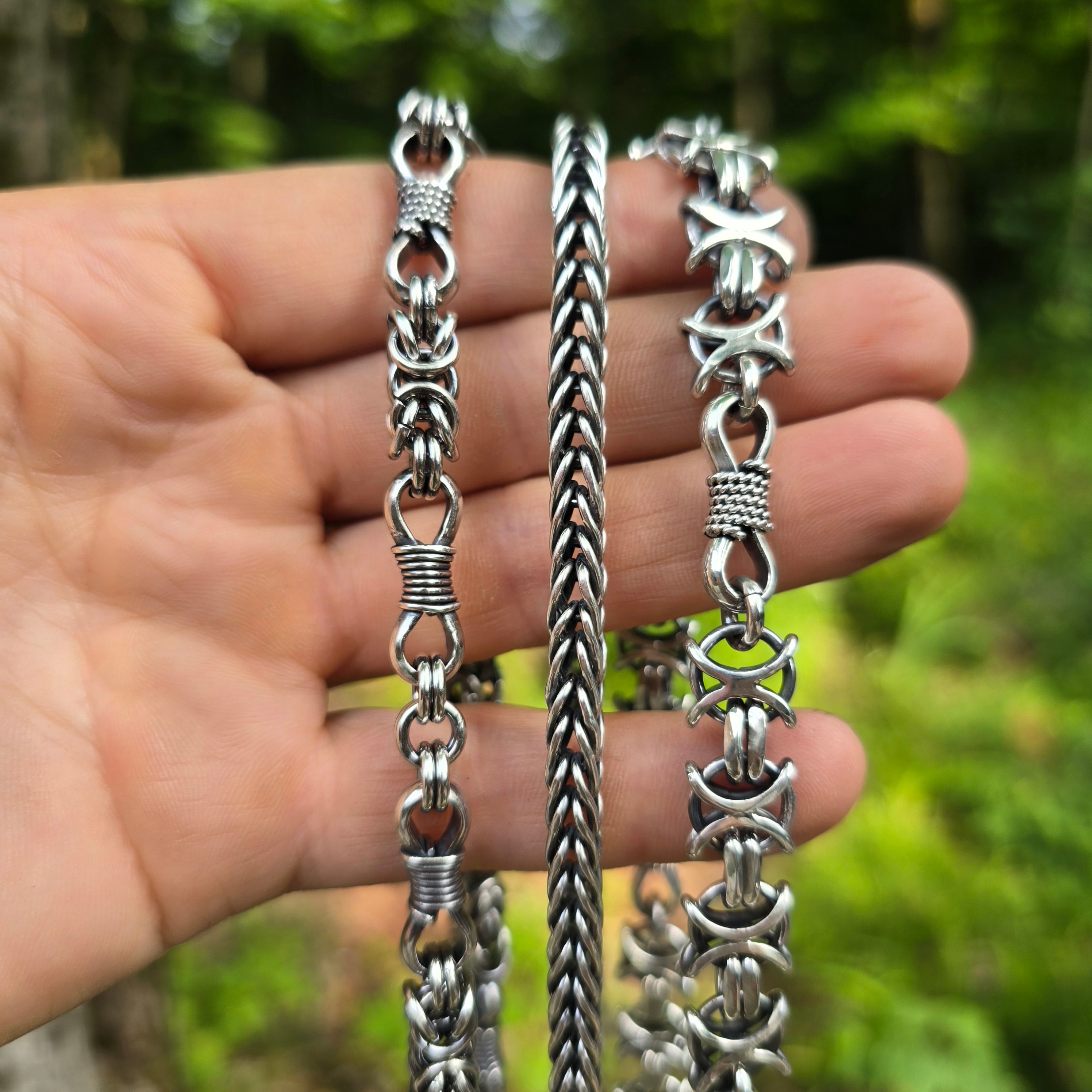 Collection of hand-forged chains displayed on hand in natural setting.