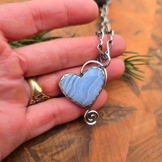 Hand-forged sterling silver crazy lace agate heart pendant displayed on hand
