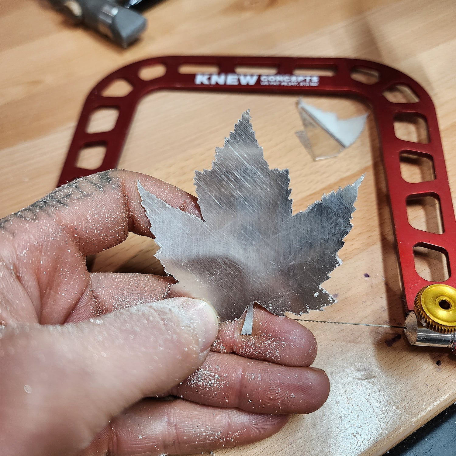 Silversmith displaying hand sawn maple leaf with coping saw and silver dust still on hands from forging jewelry.
