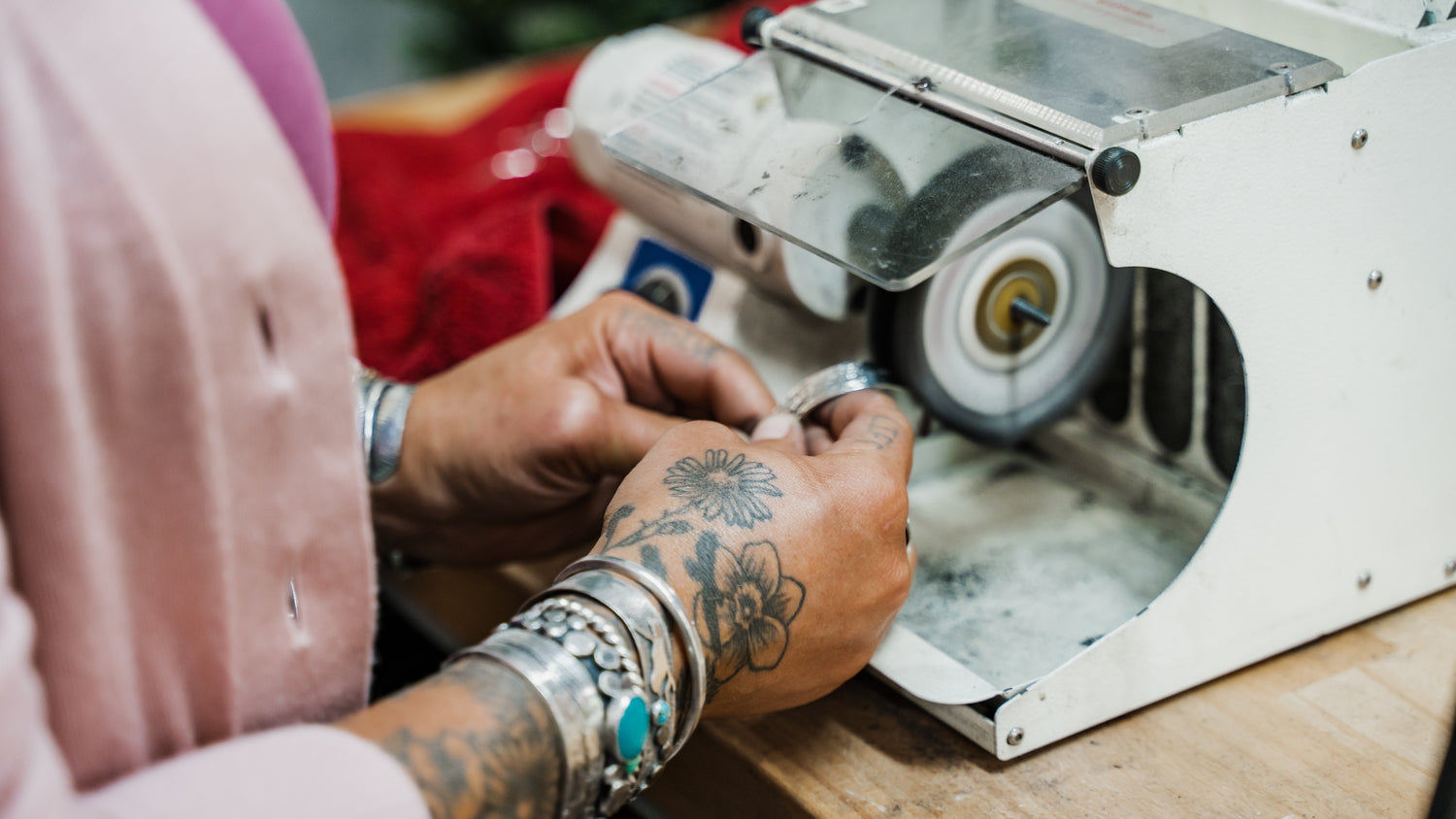 Detailed view of silversmith using buffing wheel to polish hand-forged sterling silver cuff bracelet at workbench.