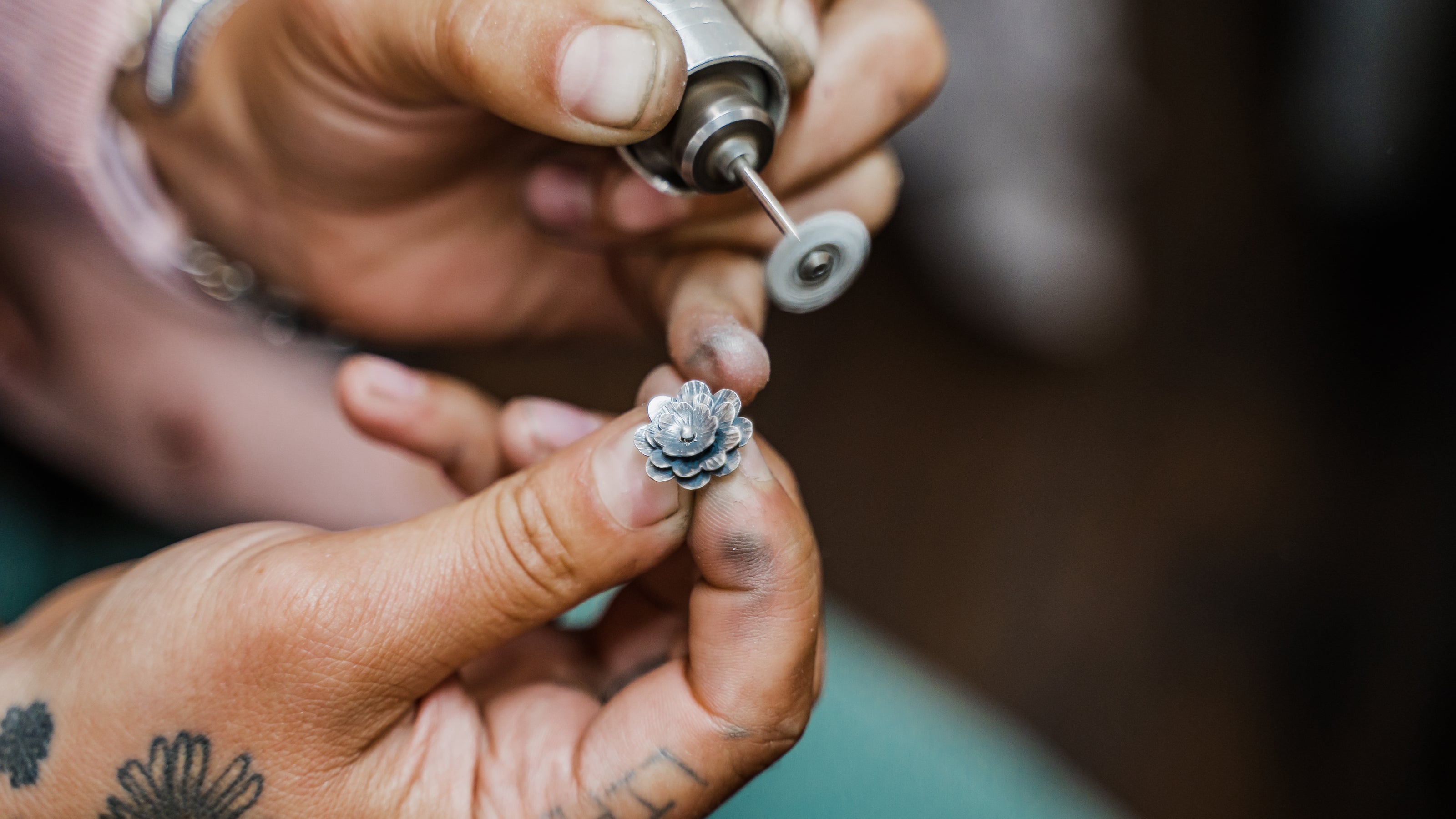 Detailed view of silversmith using flexshaft to polish a sterling silver hand-forged flower earring.