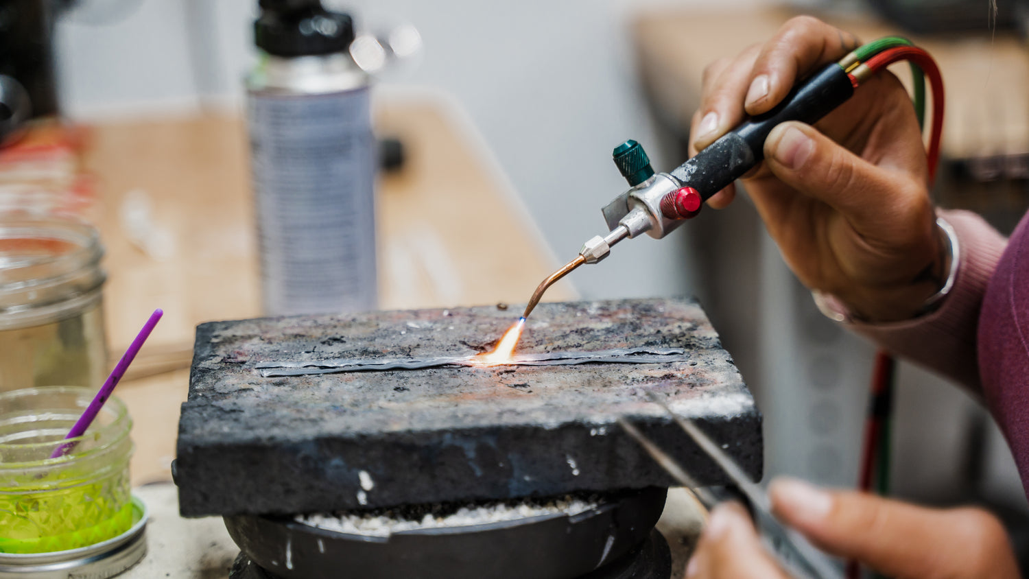 Detailed view of silversmith melting sterling silver on soldering block using smith little torch on workbench.
