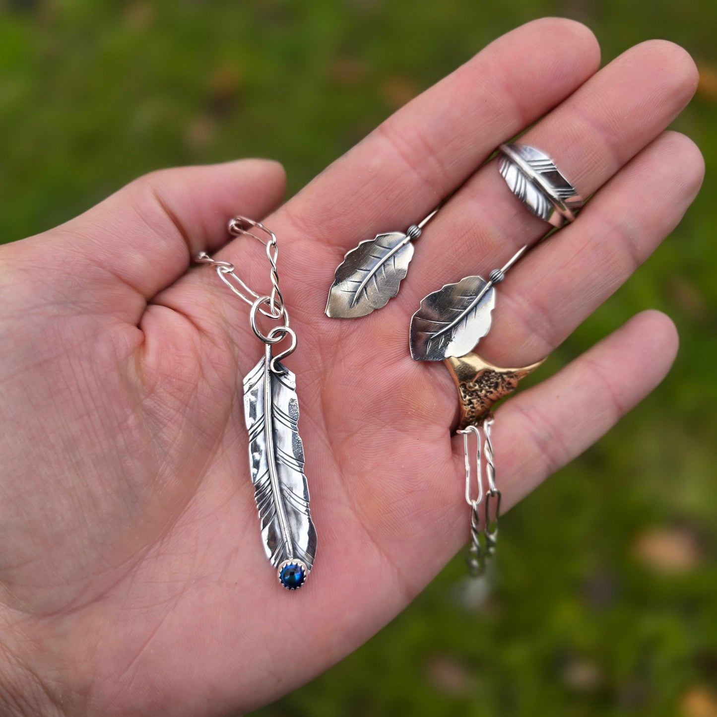 feather pendant with oil Czech glass, leaf ring, and leaf threader earrings displayed together on hand
