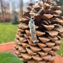 Load image into Gallery viewer, feather pendant with oil Czech glass stone set at the tip displayed on pinecone

