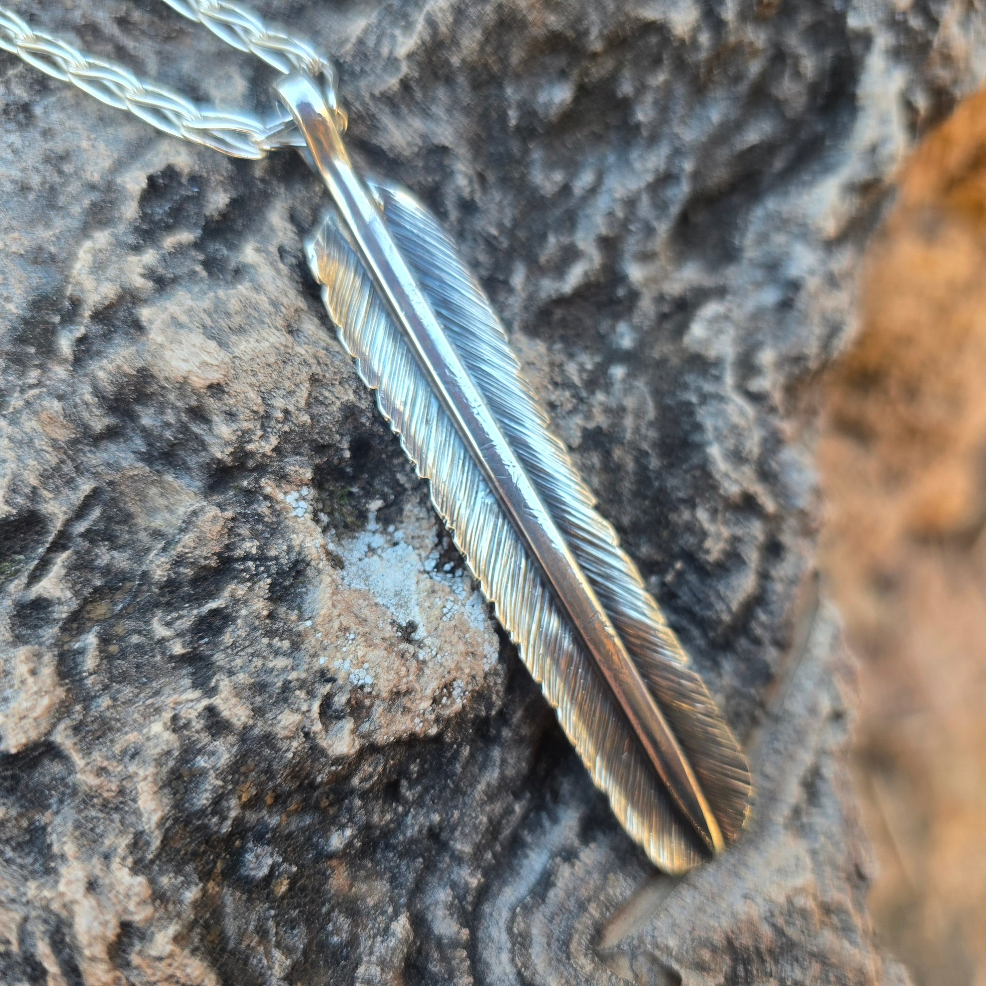 Hand stamped sterling silver feather pendant with an oxidized surface and elongated form just over three inches long.