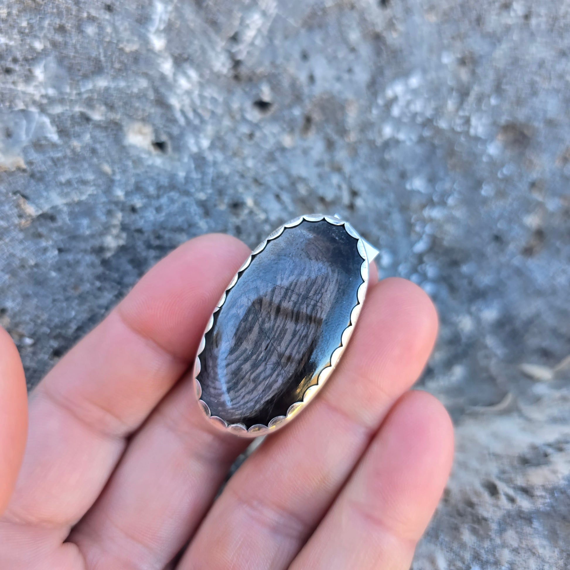 Adjustable sterling silver ring with an oval psilomelane stone just over 1.5 inches, showing scalloped bezel detail and open shank displayed on finger.