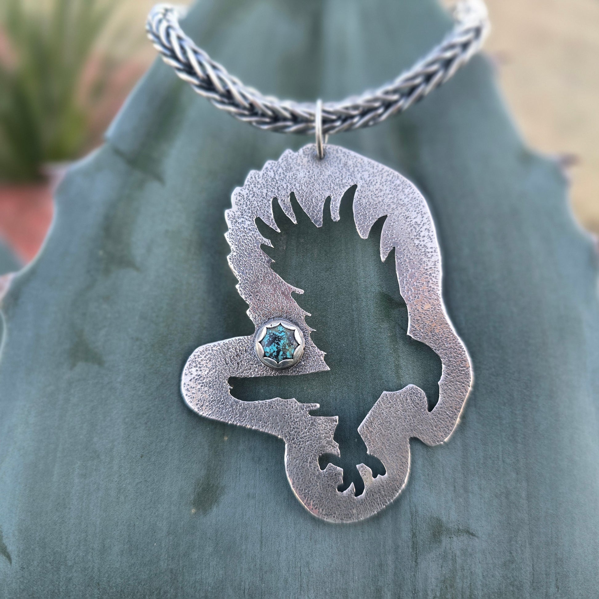 Hand-forged sterling silver raven and turquoise pendant on chain with natural background