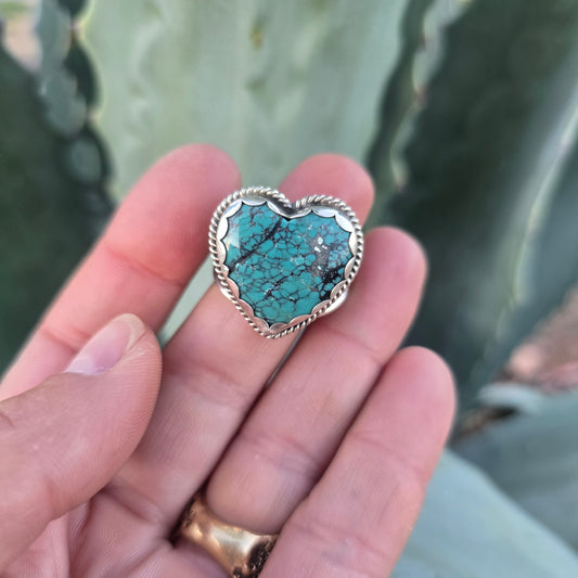 Sterling silver and turquoise heart shaped ring displayed on finger front view. 