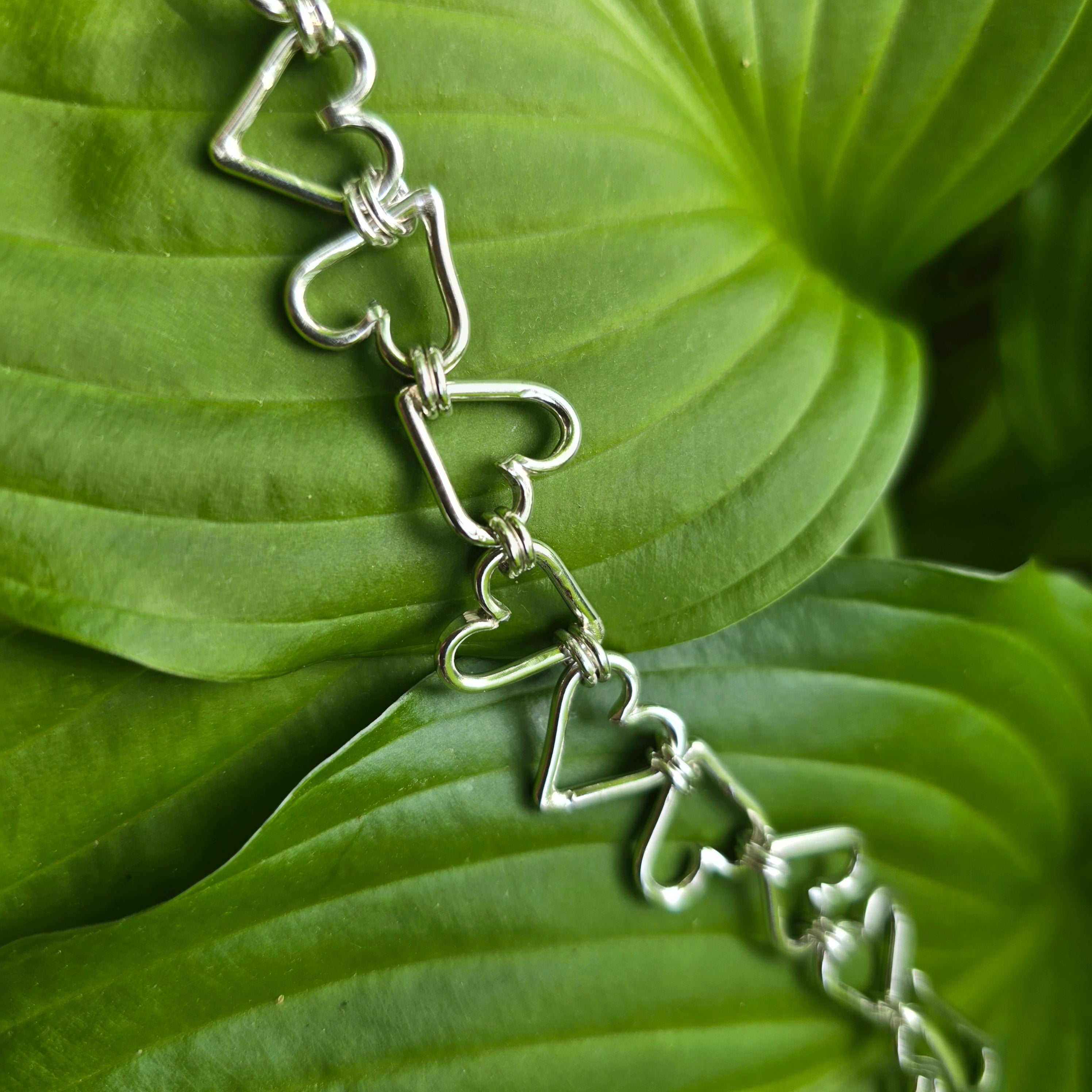 Sterling silver heart chain that was hand-forged displayed on leaf. 