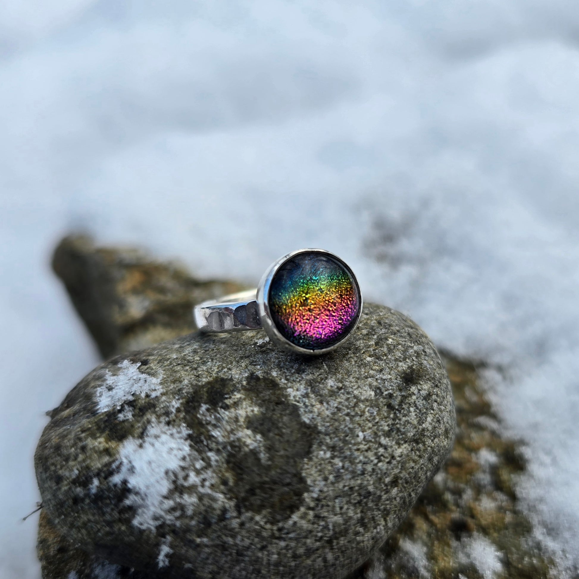 angled view of rainbow dichroic glass ring with name stamped around band