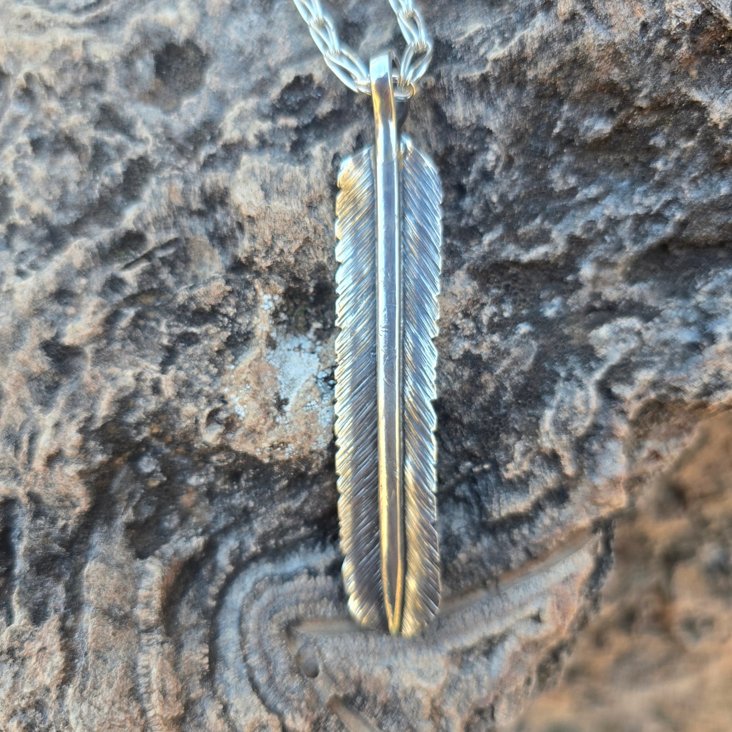 Oxidized sterling silver feather pendant formed by hand, showing stamped texture and a substantial profile.