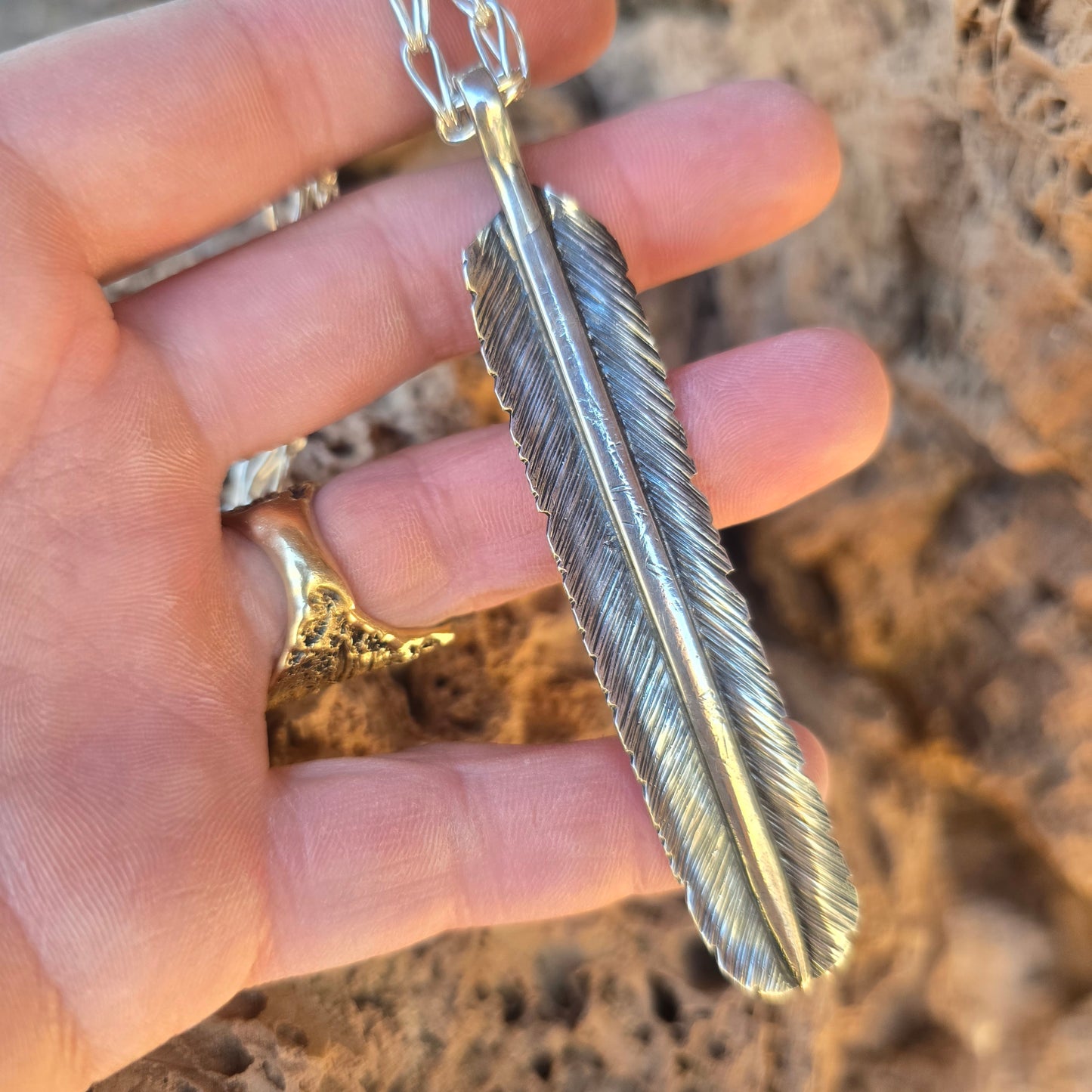 Large oxidized sterling silver feather pendant, hand stamped and shaped with visible tool marks displayed across hand.