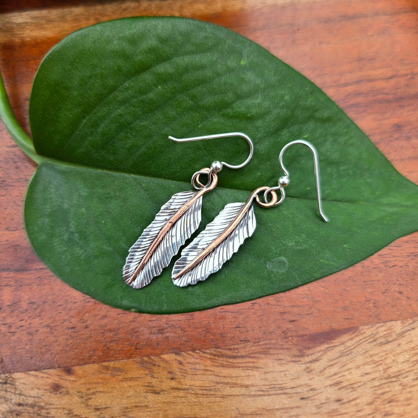 Front view of hand-forged mixed-metal feather earrings with sterling silver feathers and copper stems.