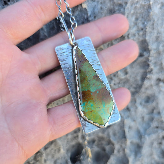Patagonia turquoise pendant measuring approximately 2.25 inches in length, showing green and brown turquoise stone set in silver, photographed on a natural surface in hand.