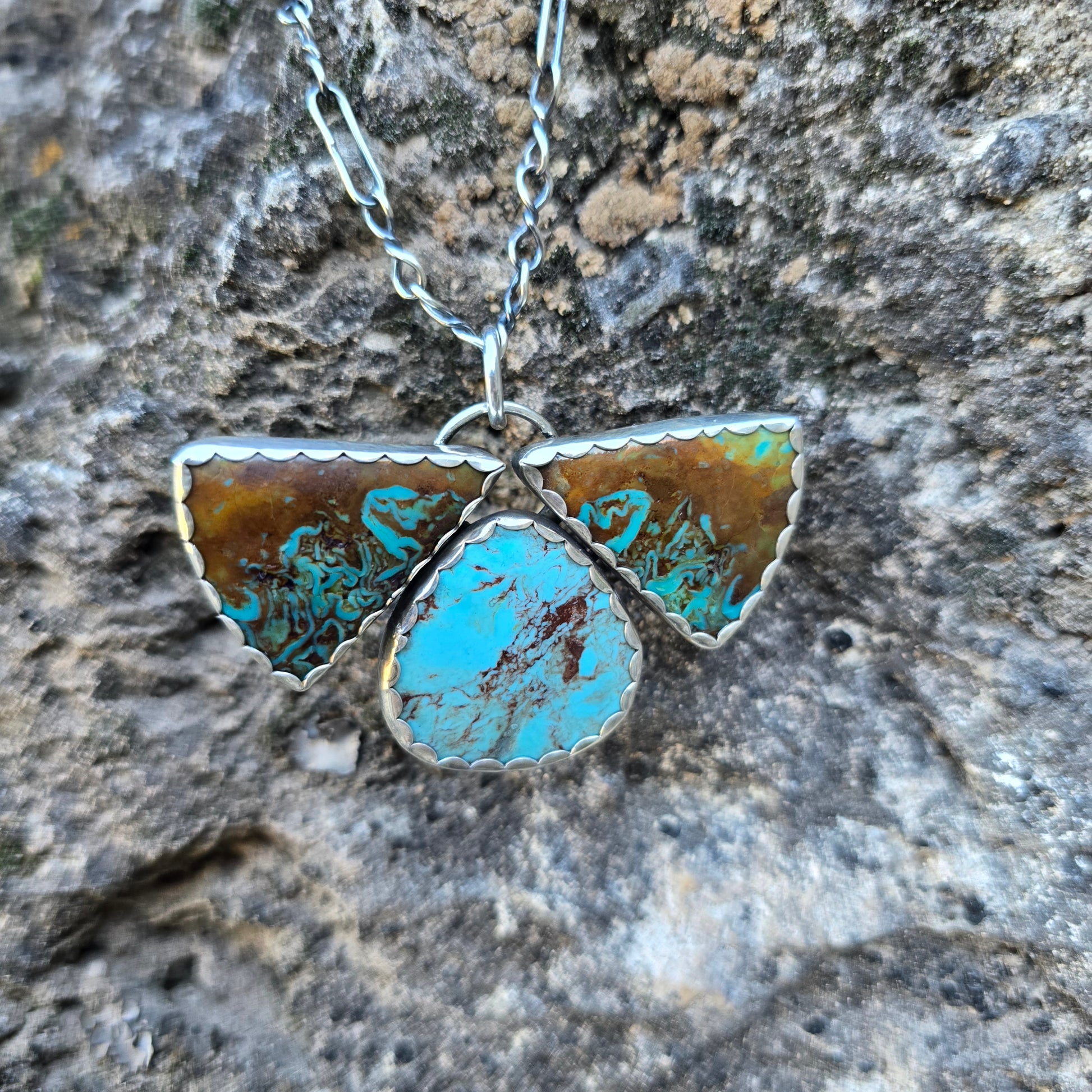 Three stone Patagonia turquoise pendant measuring about 1.75 inches, composed of two triangular stones and one oval stone set in a scalloped silver bezel.