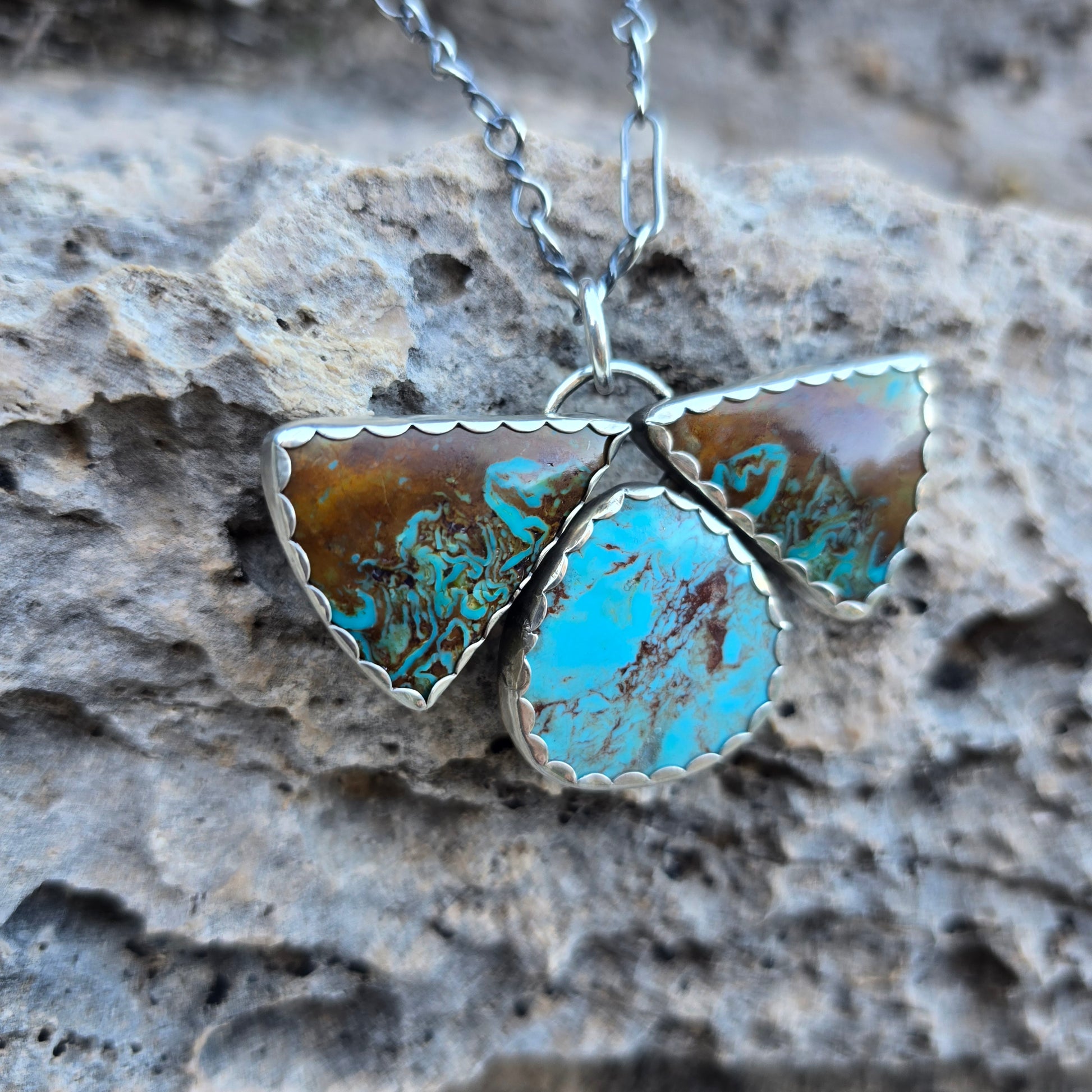 Patagonia turquoise pendant with three stones, including two triangular stones and one oval stone, blue and brown coloration visible, set in a scalloped bezel.