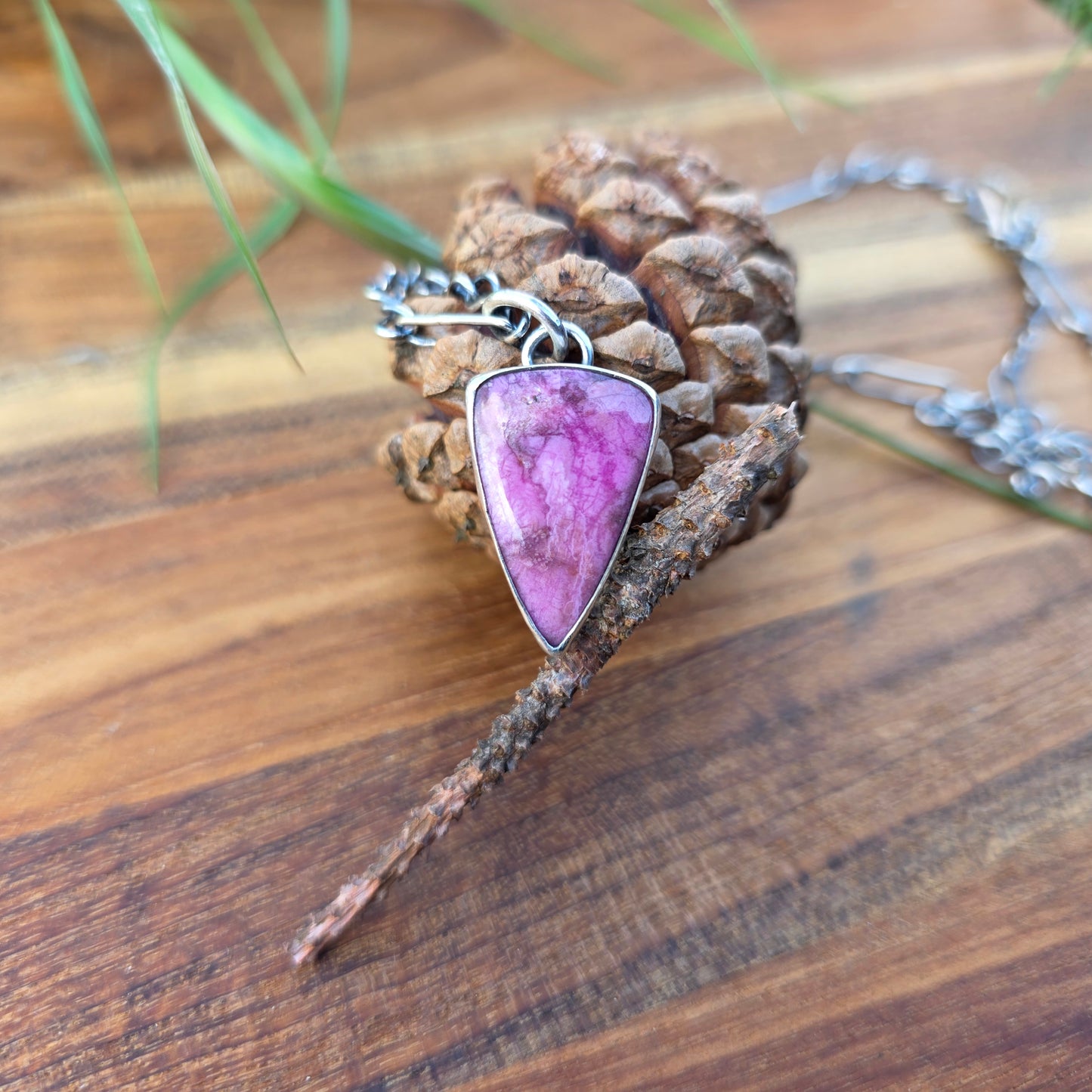Triangular cobalto calcite pendant in polished pink stone, displayed against a cactus backdrop.