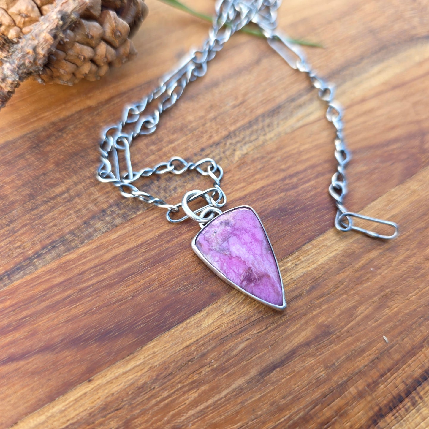Minimal display of a polished pink cobalto calcite triangular pendant resting natural background.