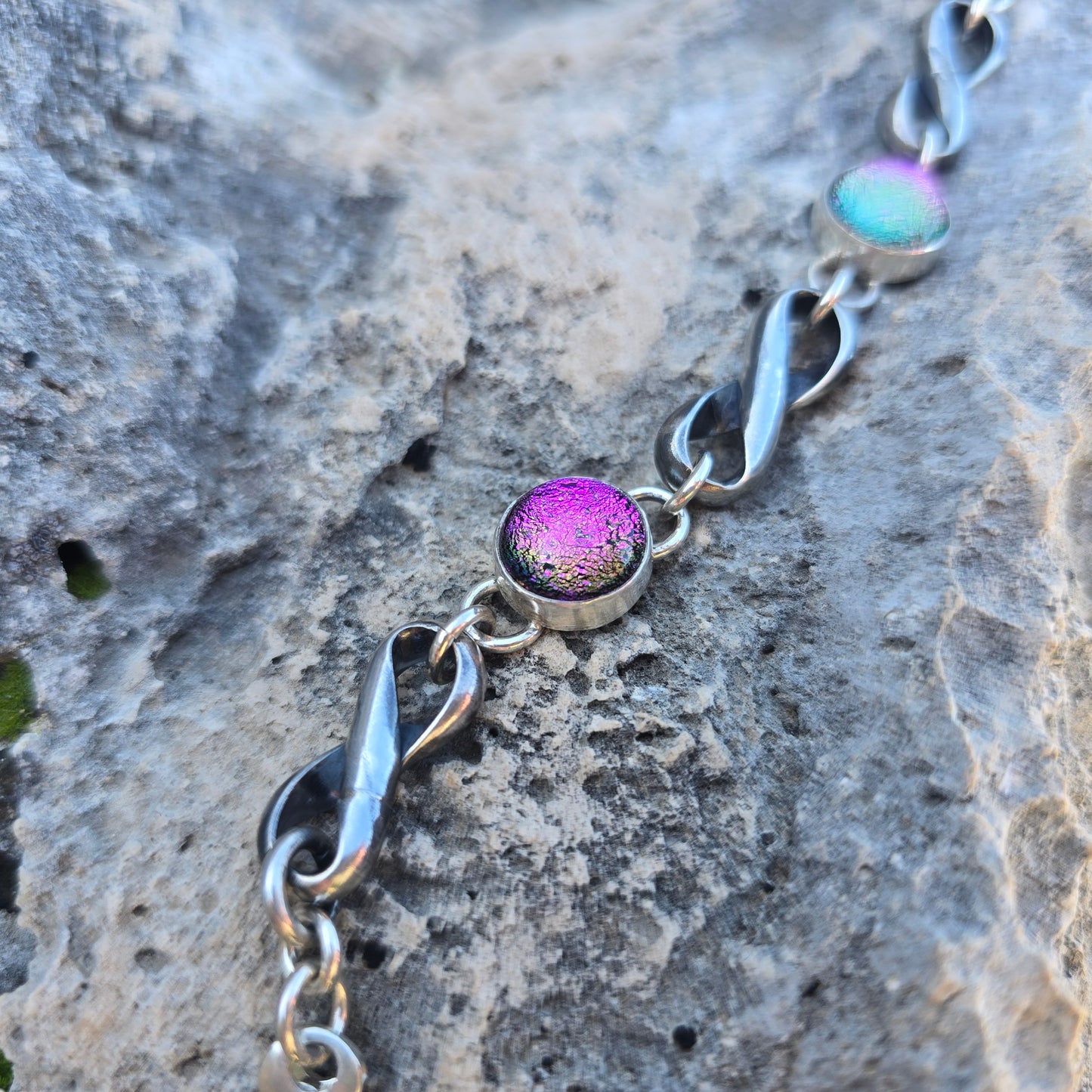 Infinity link bracelet in oxidized sterling silver with three pink dichroic glass stones set along the band detailed view.