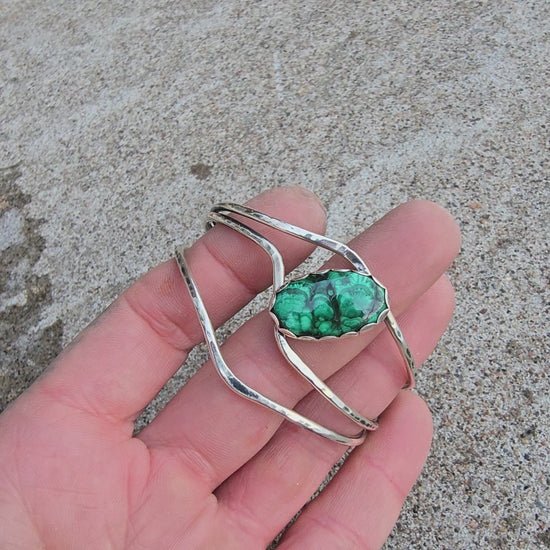 Front view of a sterling silver cuff bracelet set with an oval malachite stone and finished rotating on a hand.