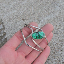 Load and play video in Gallery viewer, Front view of a sterling silver cuff bracelet set with an oval malachite stone and finished rotating on a hand.
