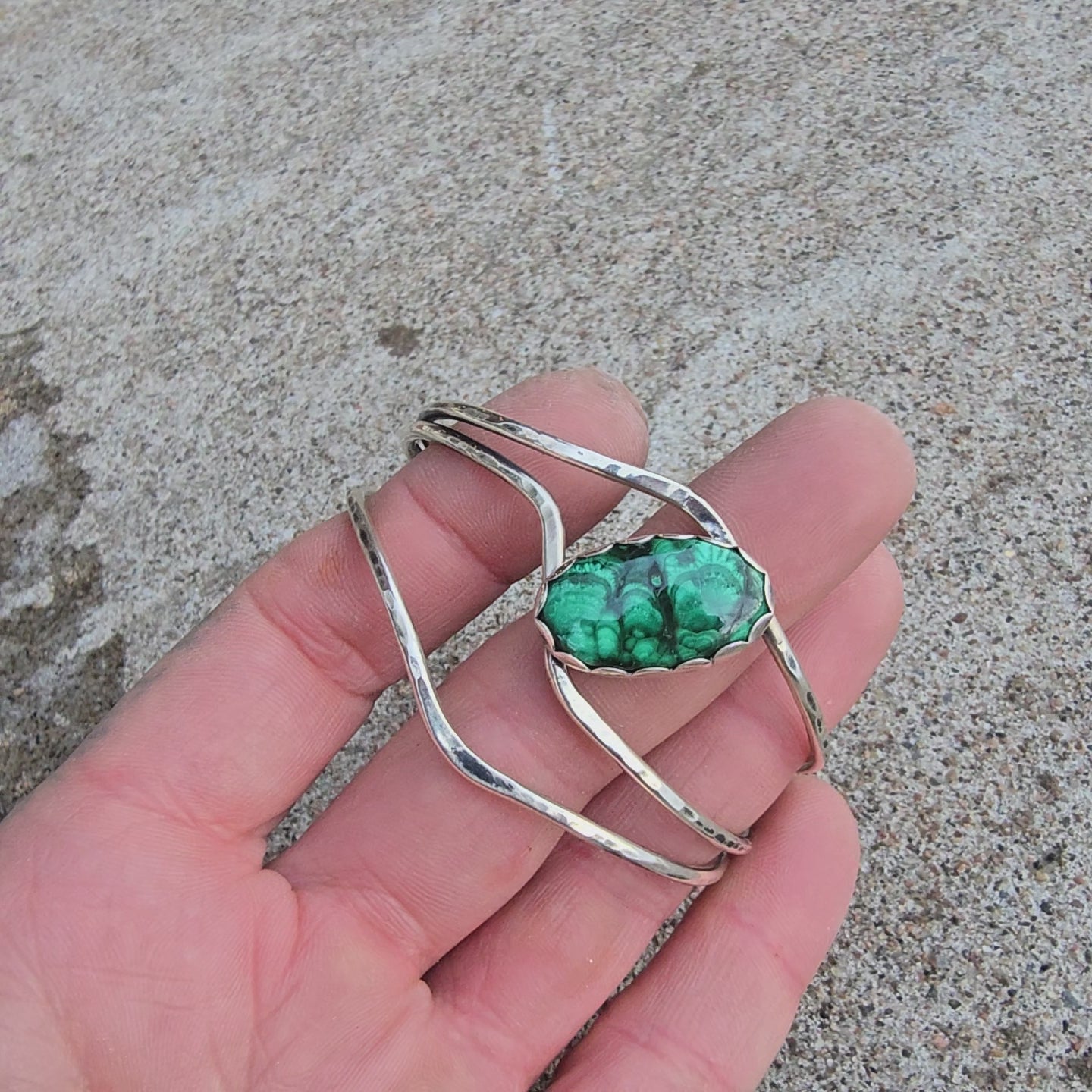 Front view of a sterling silver cuff bracelet set with an oval malachite stone and finished rotating on a hand.