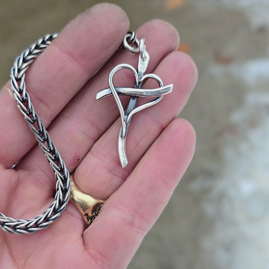 Sterling silver cross with an intertwined heart at the center, attached to a metal key ring, shown on rotating hand