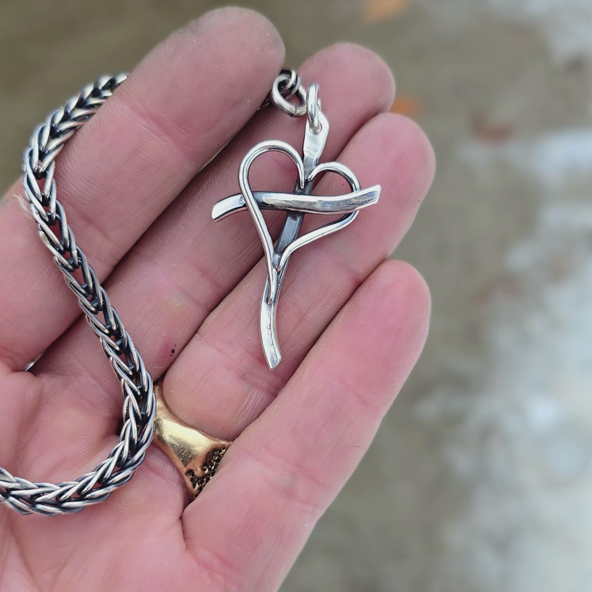 Sterling silver cross with an intertwined heart at the center, attached to a metal key ring, shown on rotating hand