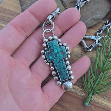 Load and play video in Gallery viewer, On-hand view of a sterling silver turquoise cross pendant showing scale, thickness, and beaded structure.
