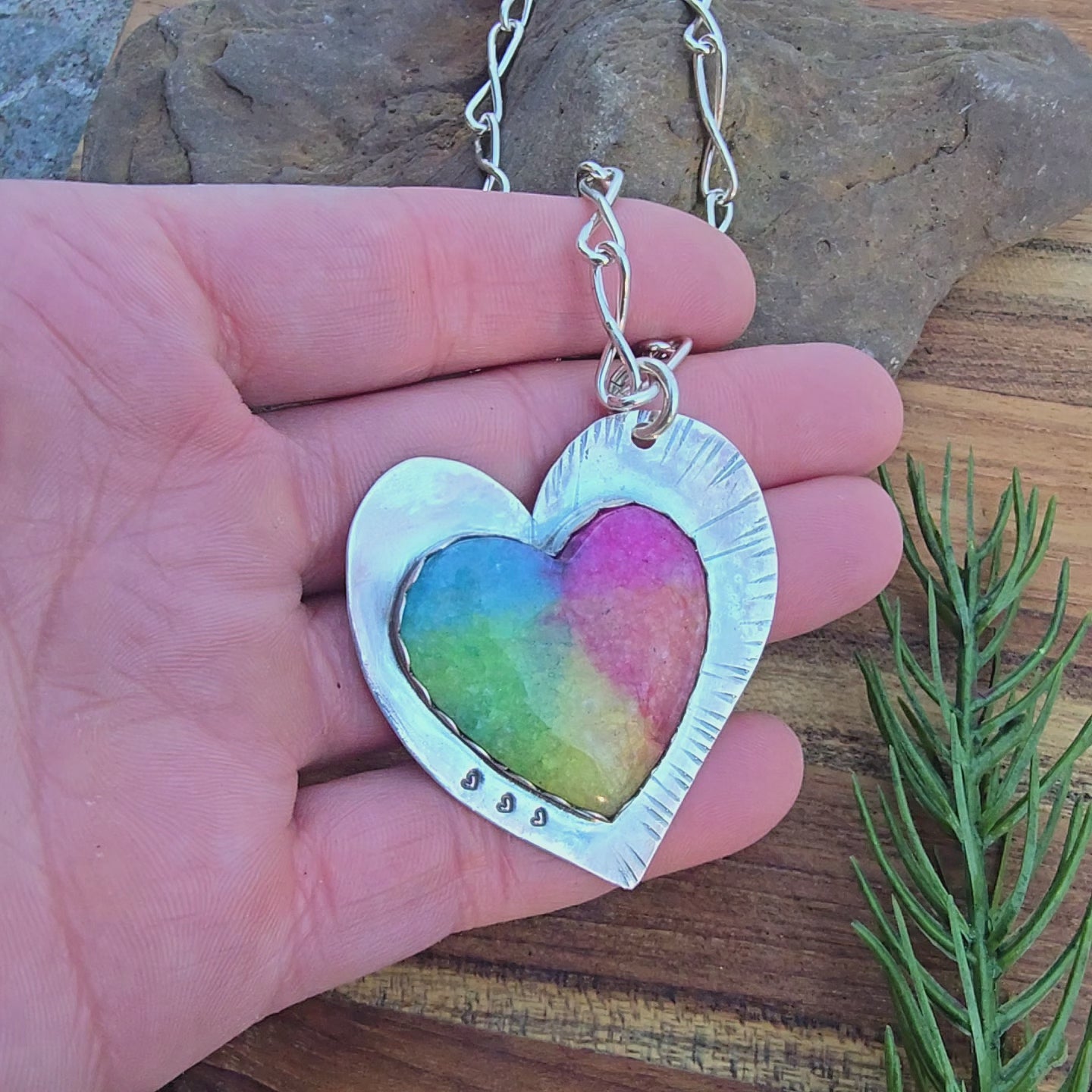 Top view of a heart-shaped sterling silver rainbow quartz pendant showing on hand rotating