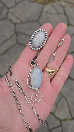 Rainbow Moonstone Collection, including moonstone threader earrings, a windswept-inspired pendant, a beaded moonstone ring, and a handmade twisted link chain.