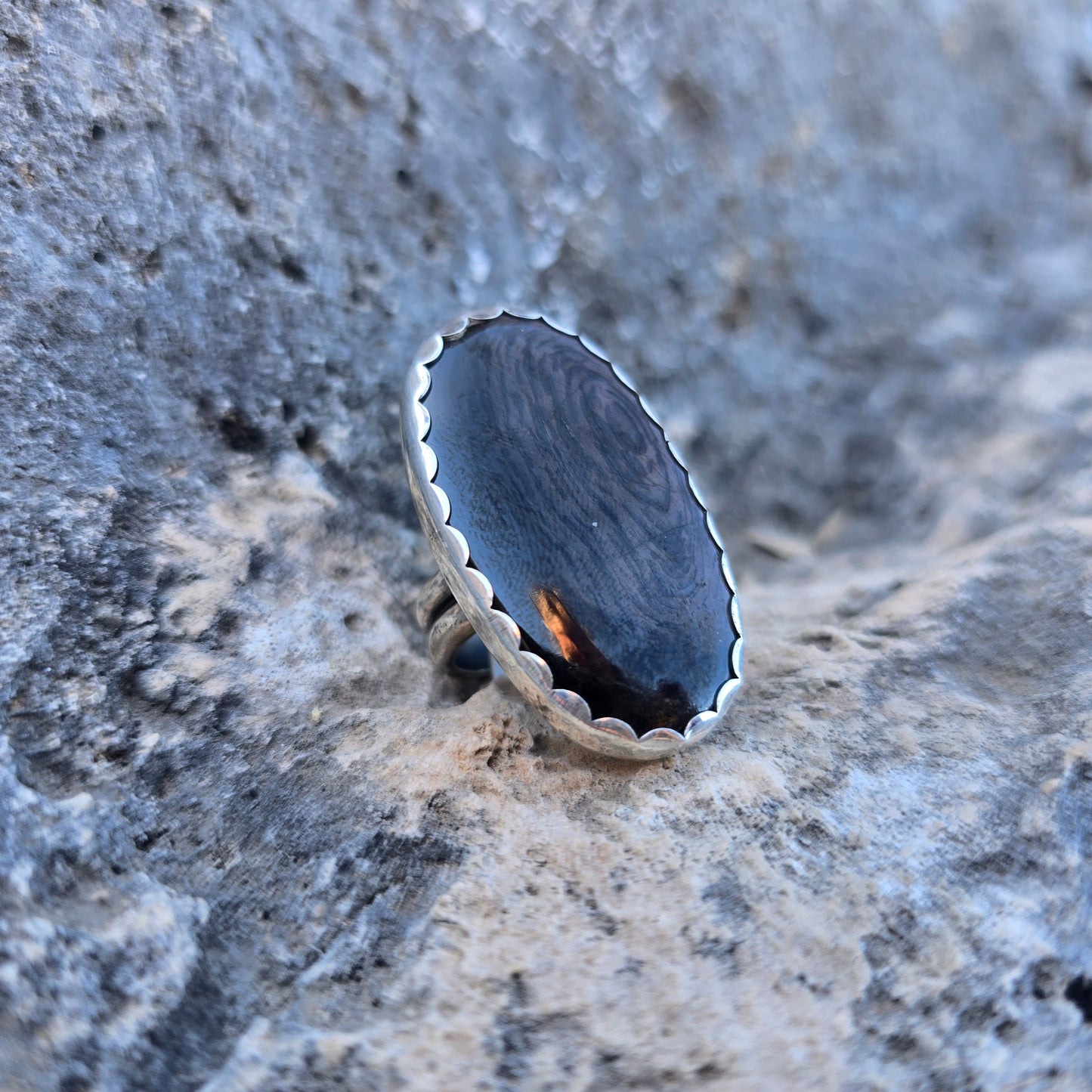 Oval psilomelane stone ring with a stone measuring just over 1.5 inches, set in a scalloped sterling silver bezel with an adjustable open band angled view.