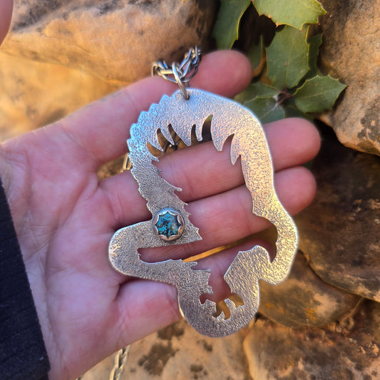 Sterling silver raven-shaped pendant with a turquoise accent, oxidized finish, and a textured surface, measuring just over 3.5 inches in length with a large bail visible.